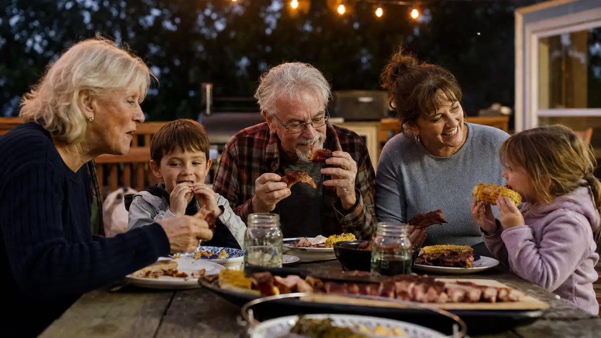Gwen, Ray, Bev, and the grandkids gathered at a long outdoor table eating smoked ribs